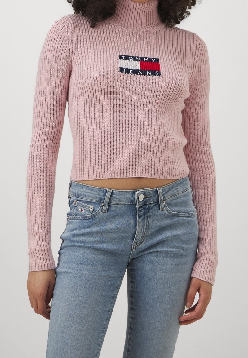 Rosa ribbad polotröja med en broderad logga i marinblått, rött och vitt. Kombinerad med ljus tvätt, högkända jeans.