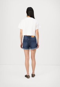 T-shirt branca cortada emparelhada com calções de ganga azul-escuro com as bainhas enroladas, dois bolsos traseiros e uma etiqueta de couro bege na cintura.