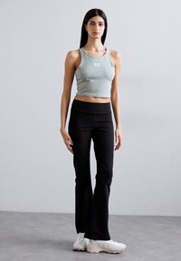 Light green cropped tank top with white logo, paired with high-waisted black flared pants and white sneakers. Smooth fabric texture visible.