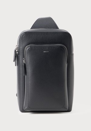 Schwarzer Rucksack aus strukturiertem Leder mit vorderer Reißverschlusstasche und silberfarbenen Reißverschlussanhängern auf schlichtem hellem Hintergrund.