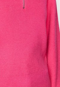 Suéter de punto de color rosa brillante con cierre de cremallera en el cuello, con un patrón texturizado y mangas largas.