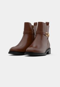 Bruine leren enkellaarzen met een zijrits, decoratieve band met gouden hardware, lage blokhak en ronde neus.