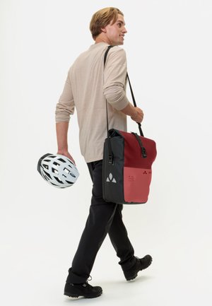 Borsa a tracolla nera e rossa con tracolla regolabile, forma rettangolare, materiale resistente, accenti grafici e design elegante. Uomo che tiene un casco bianco.