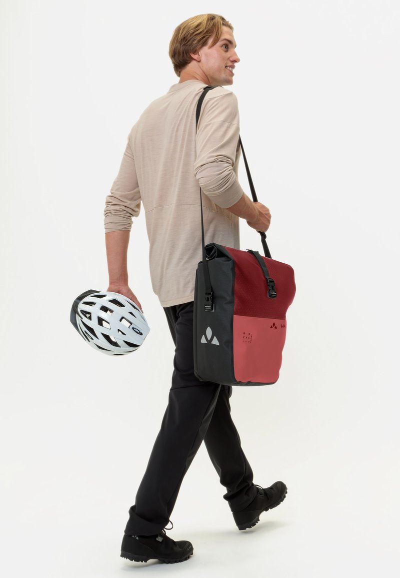 Borsa a tracolla nera e rossa con tracolla regolabile, forma rettangolare, materiale resistente, accenti grafici e design elegante. Uomo che tiene un casco bianco.