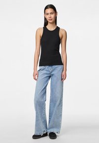 Černý žebrovaný top s kulatým výstřihem, kombinovaný se světle modrými širokými džíny a černými botami, stojící na neutrálním pozadí.