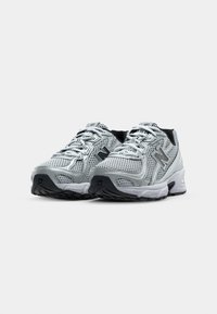 Paire de baskets de sport gris et blanc avec tissu en mesh et détails noirs sur les semelles et les côtés.