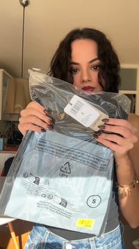 Clear plastic packaging displaying a size tag "S". Features safety warnings, recycling symbols, and a textured design on the material.