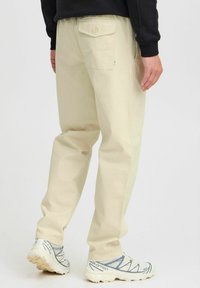 Beige chino's van katoen, met een soepele pasvorm, achterzak en contrasterende stiksels. Gemaakt in combinatie met witte sneakers.