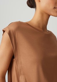 Bruine korte mouw top, gladde stof, ronde halslijn, relaxte pasvorm, zijsplit details, minimalistisch ontwerp, verfijnde kleur.