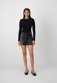 Top negro de manga larga con una costura diagonal y un sutil corte, combinado con pantalones cortos de mezclilla negros desgastados de cintura alta y planos negros.