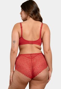 Soutien-gorge rouge et culotte taille haute. Le soutien-gorge dispose de bretelles réglables et d'une texture lisse. La culotte présente un motif de dentelle géométrique et des bords festonnés.