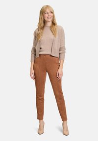 Pantalons en faux daim marron à taille haute et coupe slim, associés à un pull beige et des escarpins crème, présentant un design simple et une texture subtile.