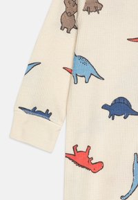 Kremna dolga majica z dolgimi rokavi, ki ima teksturirano tkanino z večbarvnimi vzorci dinozavrov in živali v modri, rdeči in rjavi barvi.