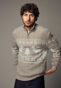 Strickpullover in hellbeige mit einem Reißverschlusskragen, der weiße Rentier- und Schneeflockenmuster über der Brust sowie strukturierte Zopfmusterdetails aufweist.