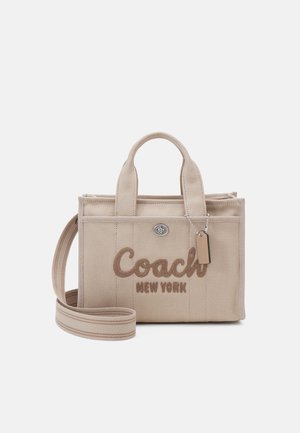Beige canvas håndtaske med broderet "Coach New York" logo, to topstænger, aftagelig rem og sølv hardware detaljer.