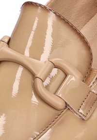 Zapato de charol beige con una hebilla decorativa, acabado brillante y diseño de punta redonda. Plantilla texturizada visible.