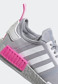 Baskets Adidas grises avec des rayures blanches, un onglet arrière rose et un bloc de semelle intermédiaire rose, présentant une tige en maille et des lacets à l'avant.