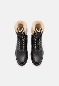 Botas de cuero negras con un cuello de borreguillo beige, diseño con cordones, ojetes en tono dorado y textura suave.