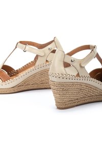 Sandales compensées en cuir beige avec des semelles en jute tressé, design à bride T, coutures décoratives et accents métalliques sur les côtés.