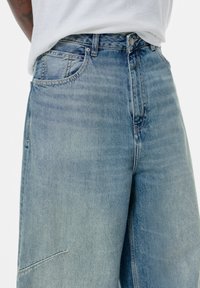 Svijetloplave traperice s visokim strukom, koje imaju klasičan dizajn s pet džepova i suptilnim izbljeđivanjem. Šivani detalji dodaju dodatnu finu notu.