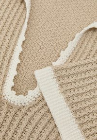 Beige gestrickter Stoff mit weißer Häkelkante, die detaillierte Texturen und Muster in Nahaufnahme zeigt.