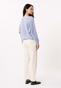 Pull en tricot bleu clair, pantalon crème à jambes droites et chaussures vertes. Le pull a une coupe ample et un motif texturé, tandis que le pantalon possède des poches arrière.