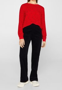 Rode langemouwtop met zwarte horizontale strepen en kleine accenten; gecombineerd met zwarte corduroy recht-pijp broeken en witte sneakers.