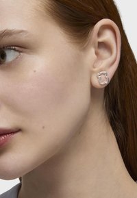 Orecchini d'argento a forma di orso, con una superficie liscia e lucida e un design semplice a contorno, indossati all'orecchio di un modello.