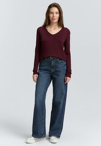 Viininpunainen pitkähihainen v-kaula-aukollinen paita yhdistettynä korkeavyötäröisiin, leveälahkeisiin sinisiin farkkuihin ja valkoisiin tennareihin, rento istuvuus ja kevyt tekstuuri.