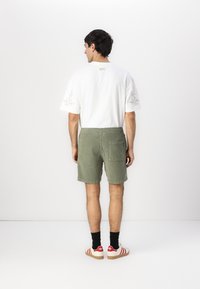 Weißes T-Shirt mit kurzen Ärmeln und hellgrünen Cordshorts, die eine Gesäßtasche haben und mit rot-weißen Turnschuhen getragen werden.