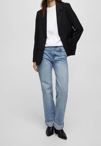 Svart skräddarsydd blazer över en vit t-shirt, kombinerad med ljusblå högmidjade jeans som är uppvikt vid fållen, och svarta ank stövlar.
