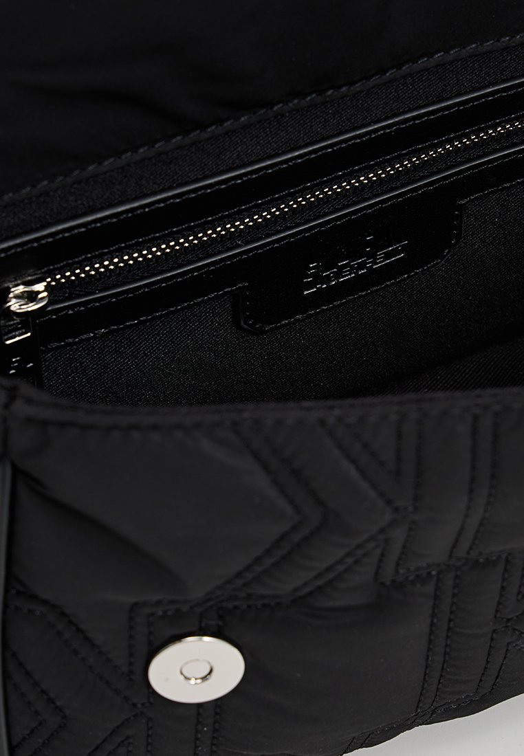 Intérieur en nylon matelassé noir avec une poche zippée, quincaillerie en argent, étiquette de logo et texture lisse. La fermeture se fait avec un bouton-pression.