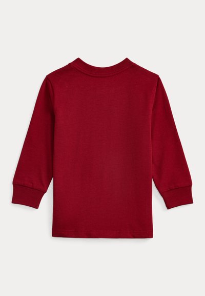 Mélyvörös hosszú ujjú ing, puha pamutból készült. Kerek nyakkivágással és bordázott mandzsettával rendelkezik. A hátulja sima, díszítés nélküli felületet mutat.