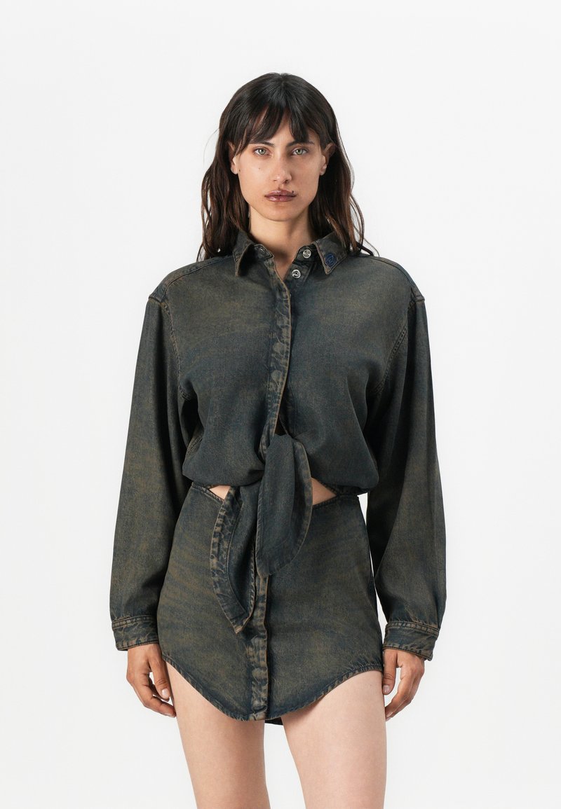Cămașă din denim închis, cu mâneci lungi, cu nasturi în față și talie legată. Asortată cu o fustă din denim care are un tiv asimetric.