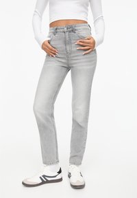 Højtaljede grå denim jeans med lige ben. Har fem lommer og knaplukning. Sammen med hvide sneakers og en tætsiddende top.