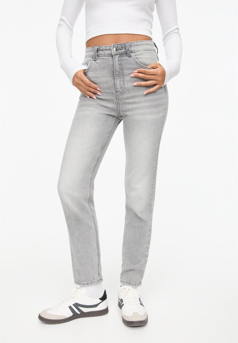 Højtaljede grå denim jeans med lige ben. Har fem lommer og knaplukning. Sammen med hvide sneakers og en tætsiddende top.