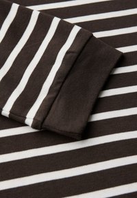 Tissu rayé brun et blanc avec une texture douce. L'image montre un gros plan d'un poignet de chemise, présentant des rayures et des coutures nettes et régulières.