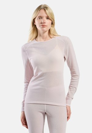 Blonde woman wearing a light pink long-sleeve top and matching leggings, standing against a plain white background.