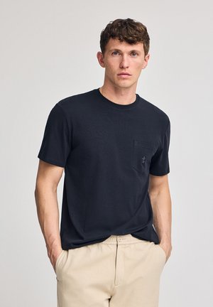 Donker marineblauwe T-shirt met korte mouwen, ronde hals en een borstzak. Gemaakt van zachte stof, met een klein logo op de zak.
