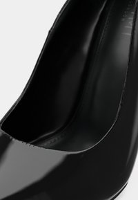 Black patent leather high heel with a smooth, glossy finish. Features a rounded toe and a low-cut vamp design. Minimal stitching detail.