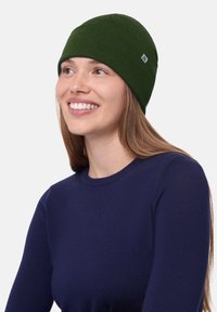 Berretto di maglia verde con un design senza cuciture, texture morbida e una piccola etichetta di marchio. Indossato da una persona con capelli lunghi.