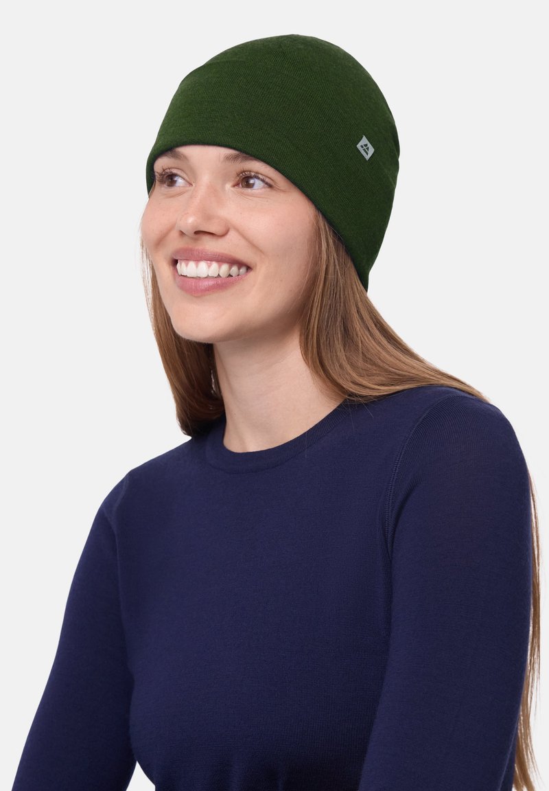 Berretto di maglia verde con un design senza cuciture, texture morbida e una piccola etichetta di marchio. Indossato da una persona con capelli lunghi.