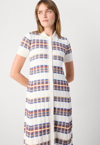 Φόρεμα μέχρι το γόνατο με κοντά μανίκια, που διαθέτει λευκή ριγωτή υφή με καρό σχέδια σε μπλε, κόκκινο και πορτοκαλί χρώμα, και κουμπιά μπροστά.