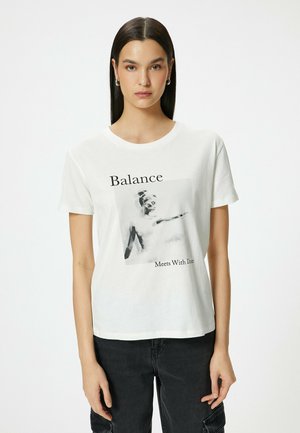 Witte katoenen t-shirt met een fotografische print van een figuur met de tekst "Balance Meets With Die" in het zwart. Korte mouwen en ronde hals.