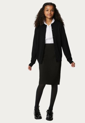 Sort cardigan med knapper, hvid skjortekrave, sort blyantskirt, sorte strømpebukser og glinsende sorte sko. Præsentation af hele outfittet.