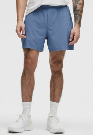 Pantaloni sportivi blu, tessuto leggero, vita elastica, lunghezza sopra il ginocchio, texture liscia, abbinati a scarpe da ginnastica bianche e calze.
