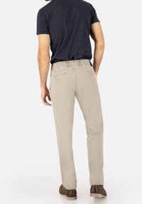 Beige chinos with a smooth texture, rear pockets featuring yellow hardware, paired with a navy t-shirt and brown shoes.