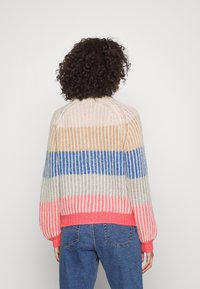 Pruhovaný svetr v pastelových barvách: béžová, modrá a korálová, s ribbovanou texturou. Má volný, boxy střih a balónové rukávy.