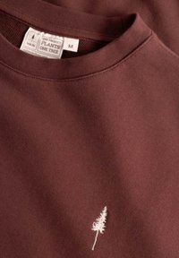 Bruine sweatshirt met een ronde hals en een klein wit geborduurd boom ontwerp. Gemaakt van zachte stof met een textuurfinish.
