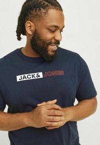 Tamsiai mėlynas medvilninis marškinėliai, ant kurių priekyje užrašytas ryškus baltas ir raudonas tekstas 'JACK & JONES'. Trumpomis rankovėmis ir apvaliu iškirpimu.